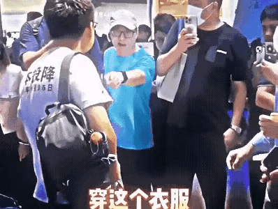 小伙子穿一件T恤衫，T恤上印的文字也很正常，但这个戴帽子的人偏偏站出来，横挑鼻子