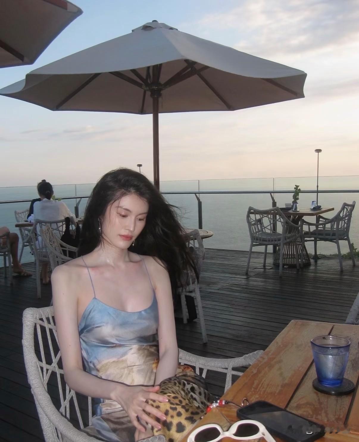 何穗海边露台超模身材太绝了一身艺术印花吊带长裙，丝滑缎面材质泛着柔和光泽，色