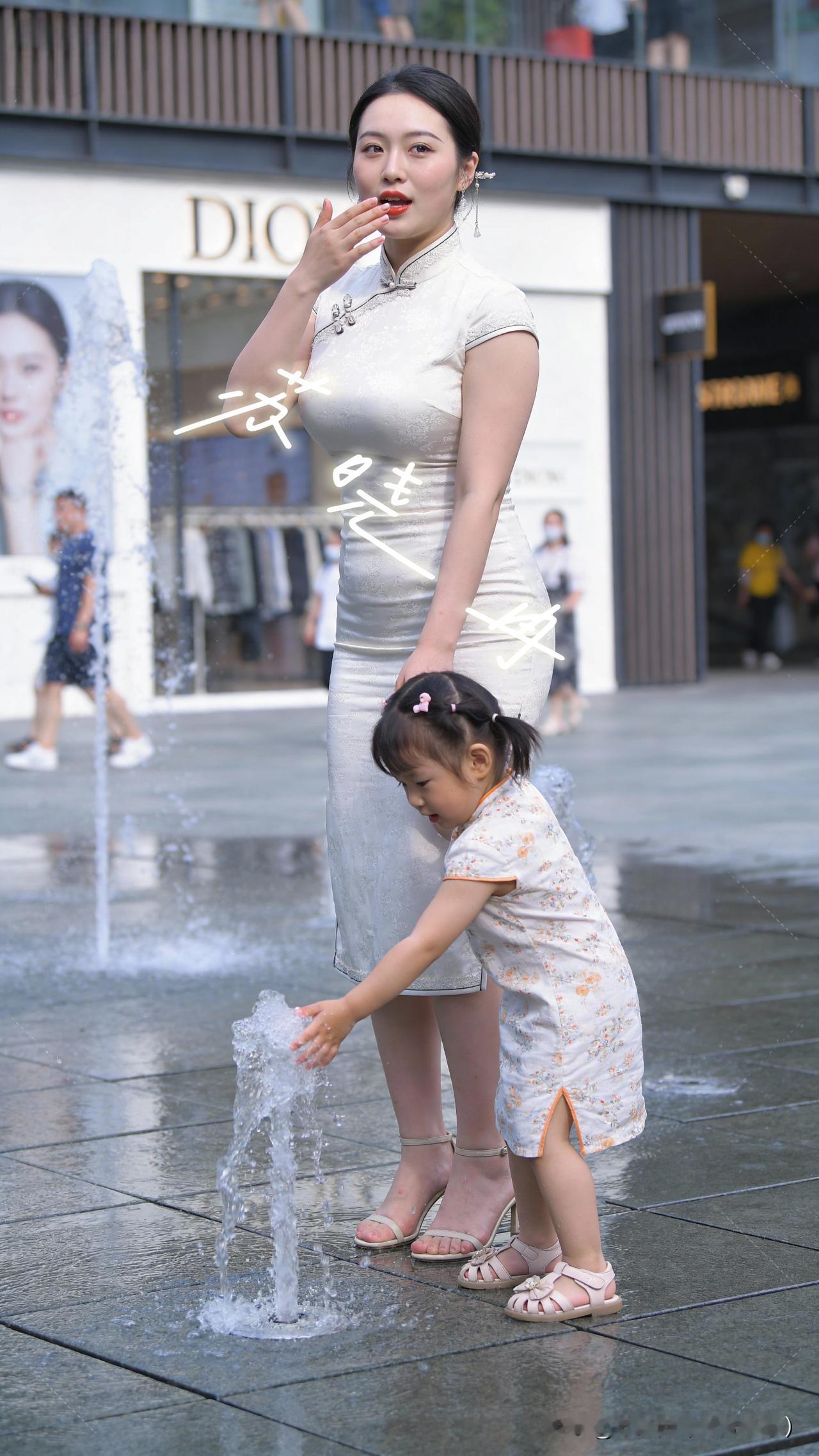 喷泉的水花在夏日里跳着灵动的舞，画面里的小丫头踮着脚、伸着小手去撩那清凉的水丝。