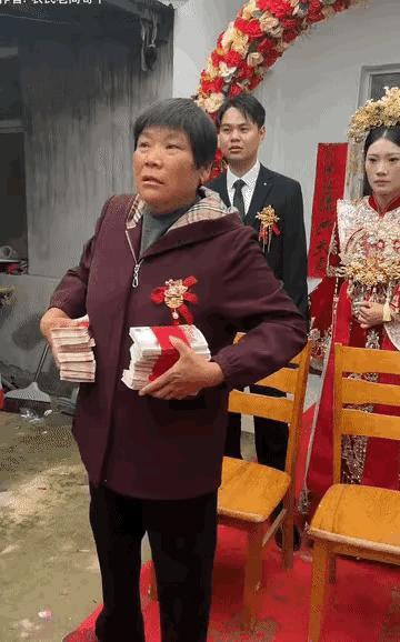 婚礼现场新娘的妈妈双手拿着两摞钱，高高的举起问现场的亲朋好友们：生女儿好不好？
