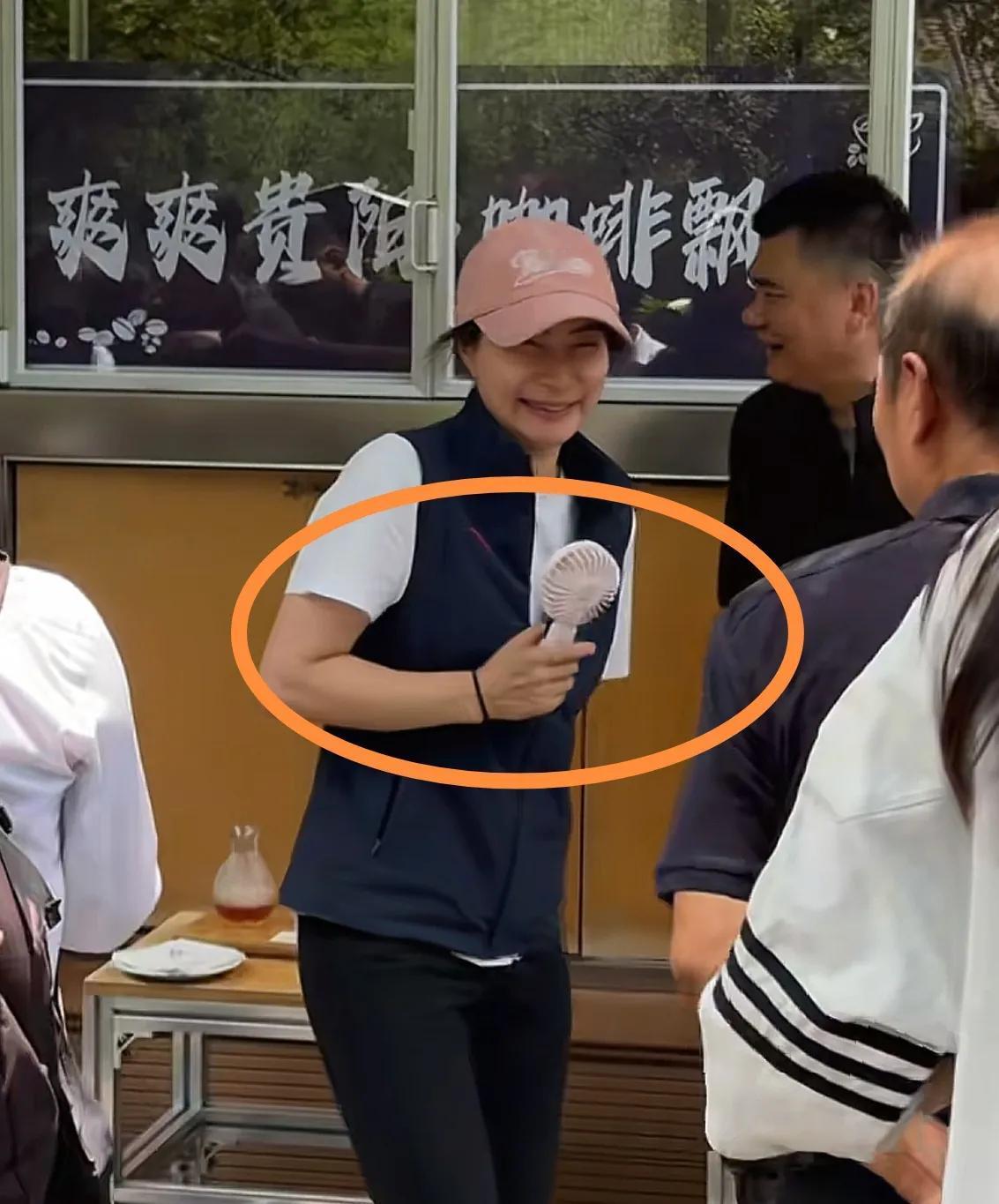 郭晶晶在贵州三都室外喝咖啡，她手里还拿了一个便携式的小风扇，一直对着自己吹。
