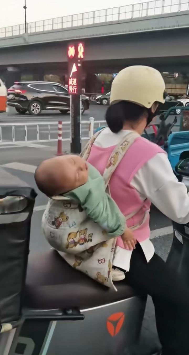 这大冷天的，一位年轻的妈妈背着熟睡中的宝宝送外卖，穿行在城市街道上，那画面，真的