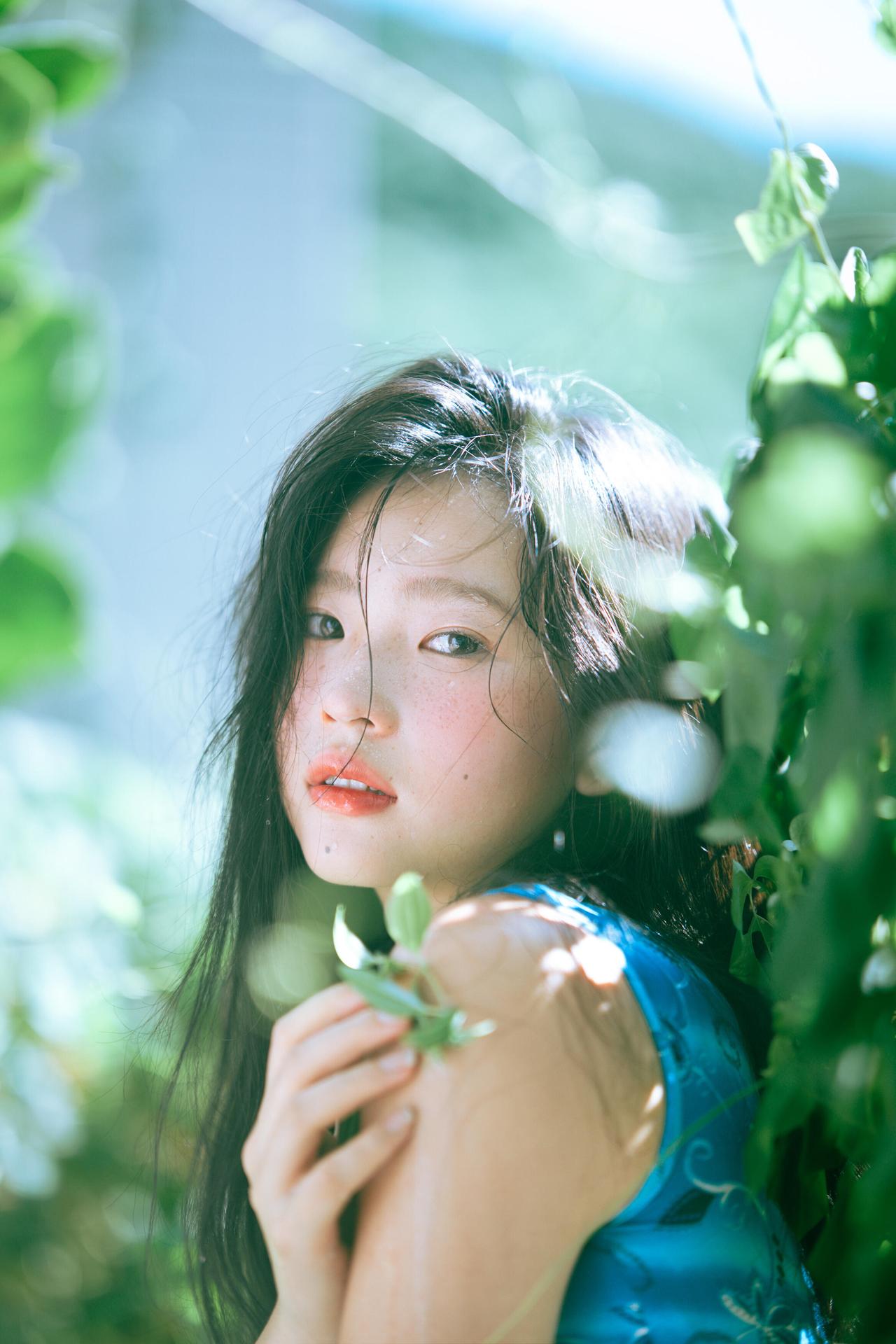 画面里，少女侧靠在花丛中，单手撑着脸颊，眼神放空，仿佛沉浸在自己的世界里。背景的