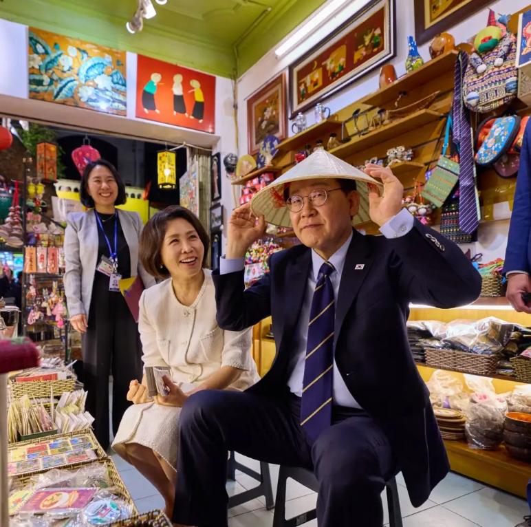 4月23日李在明在越南逛街时走进一家小店，拿起斗笠戴在头上，认真调整帽檐的模样，