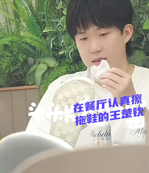 王楚钦到达机场在餐厅休息，突然一个镜头拍到他不拘小节的拿起拖鞋在擦