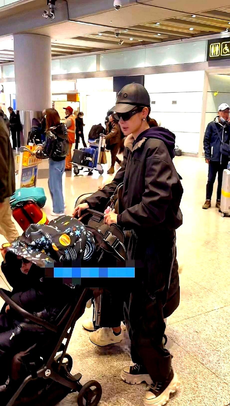 戚薇嘴唇发白，身体前倾着硬扛两个孩子。机场里，她一个人推着婴儿车，儿子在