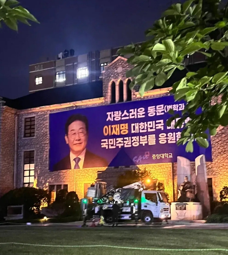 李在明当选总统后，其母校中央大学耗费巨资制作海报以表祝贺。其中有一幅覆盖大楼墙