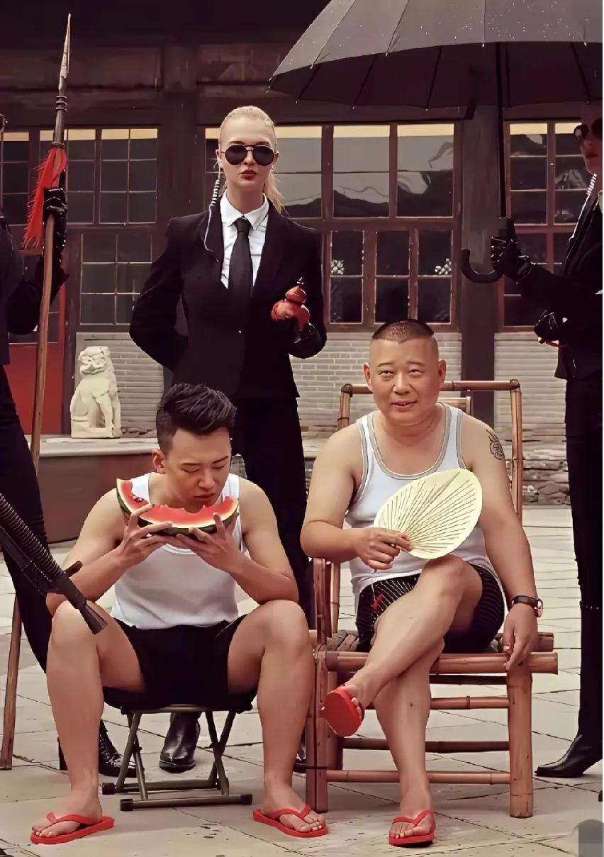 郭德纲和儿子郭麒麟的合影。父子俩穿着挎带儿大背心，脚蹬红色的拖鞋，郭麒麟低头忙