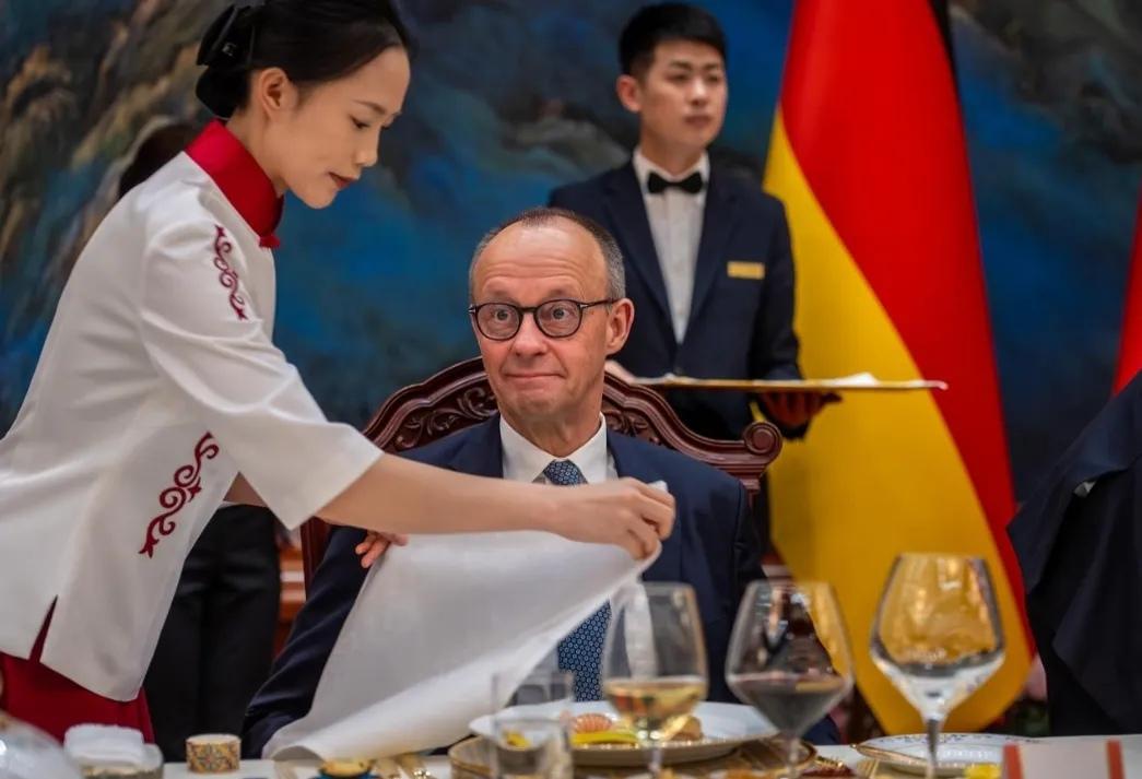 这个画面蛮有意思的！拍的是德国总理默茨在访华期间的欢迎晚宴。一边是穿着传统中