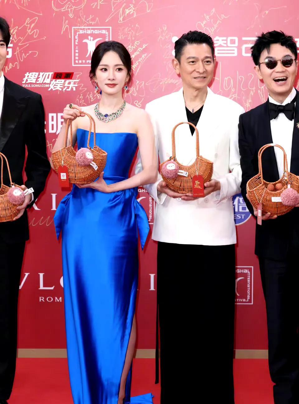 刘德华杨幂世纪同框引热议上影节红毯，杨幂身着蓝色礼服气质出众，手拿荔枝道具别具