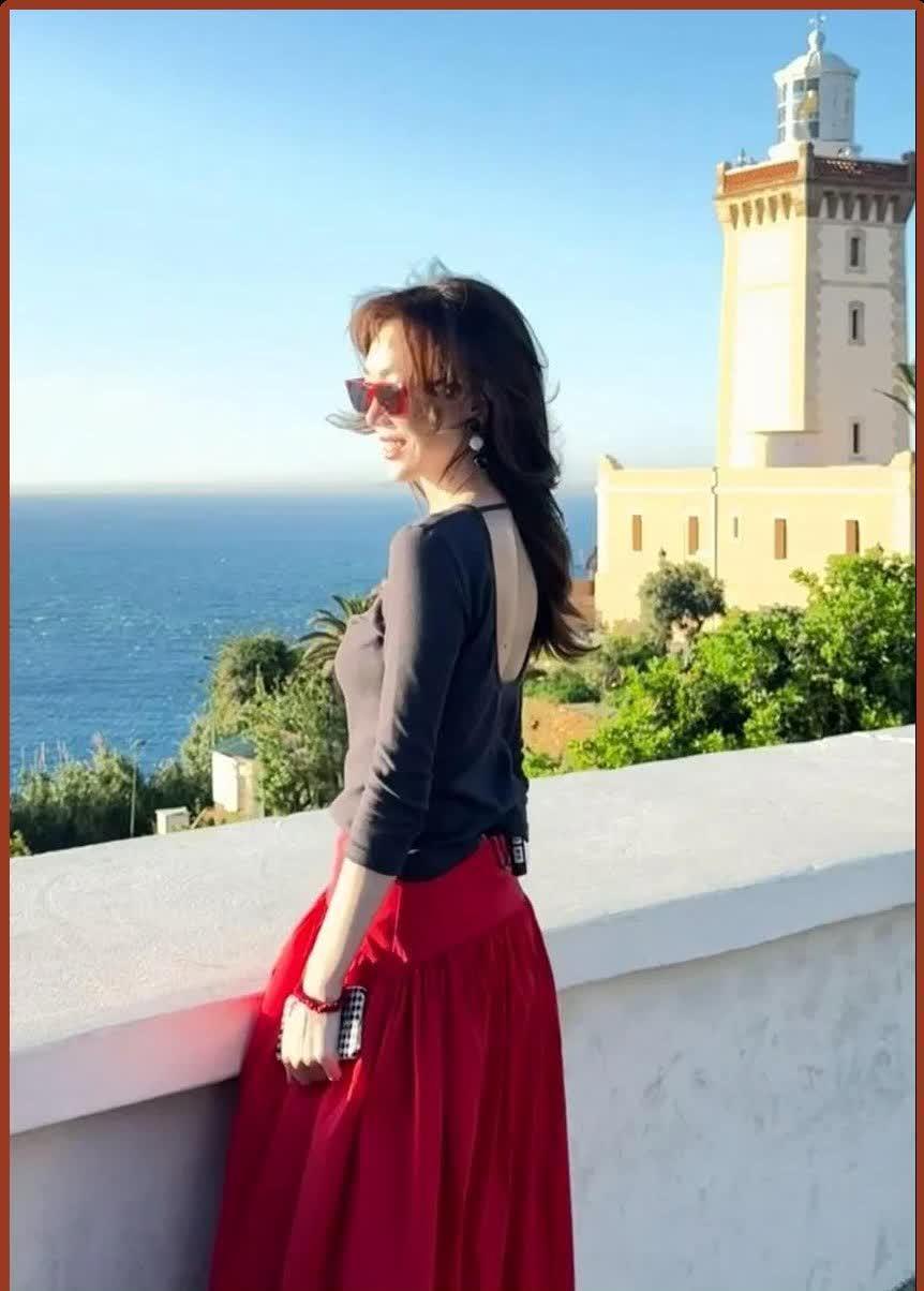 39岁的姜妍在海边身着黑色T恤和红色裙子，令网友们赞叹不已：这哪里像是在上班，分