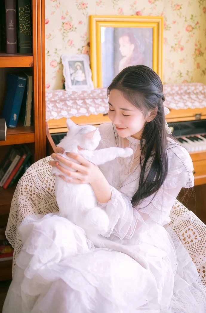 刘浩存白纱轻裹，指尖抚过猫咪软绒的毛，笑意漫过碎花墙纸，连时光都在这一刻变得温