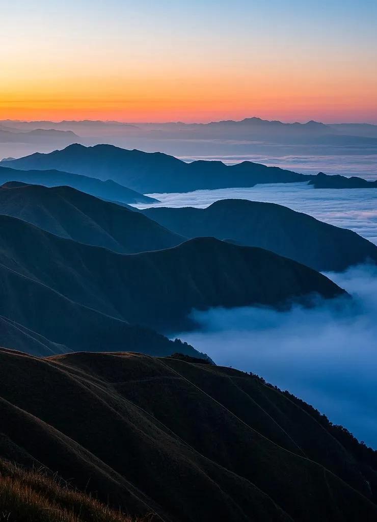 武功山的山峦被夕阳勾勒，起伏曲线与湛蓝天空映衬，山腰间云雾缥缈，似梦幻仙境。武功