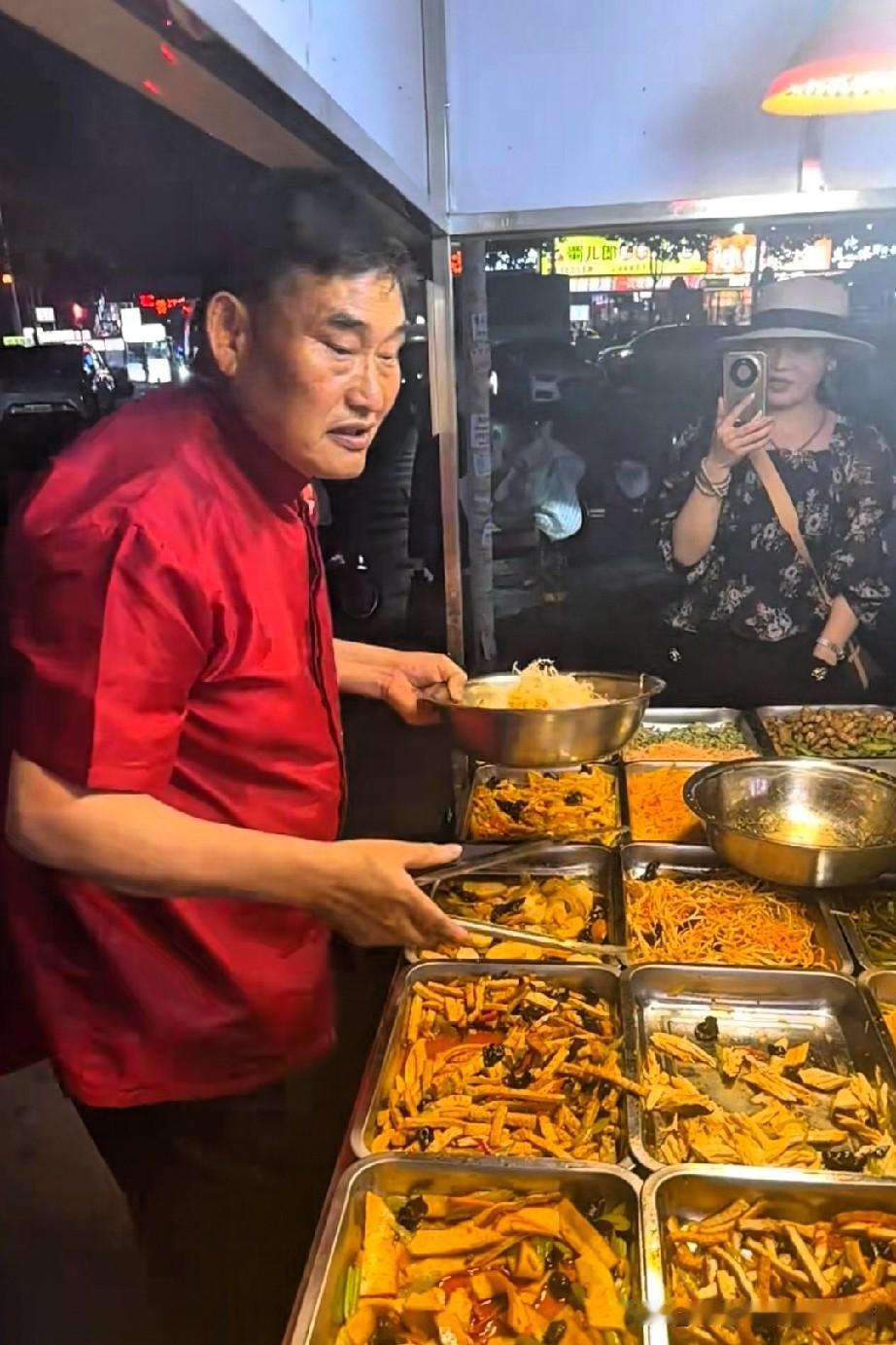 大衣哥朱之文在小吃摊上挑选凉菜，他每样菜都夹了一些，直到装了满满一大盆。大衣哥虽