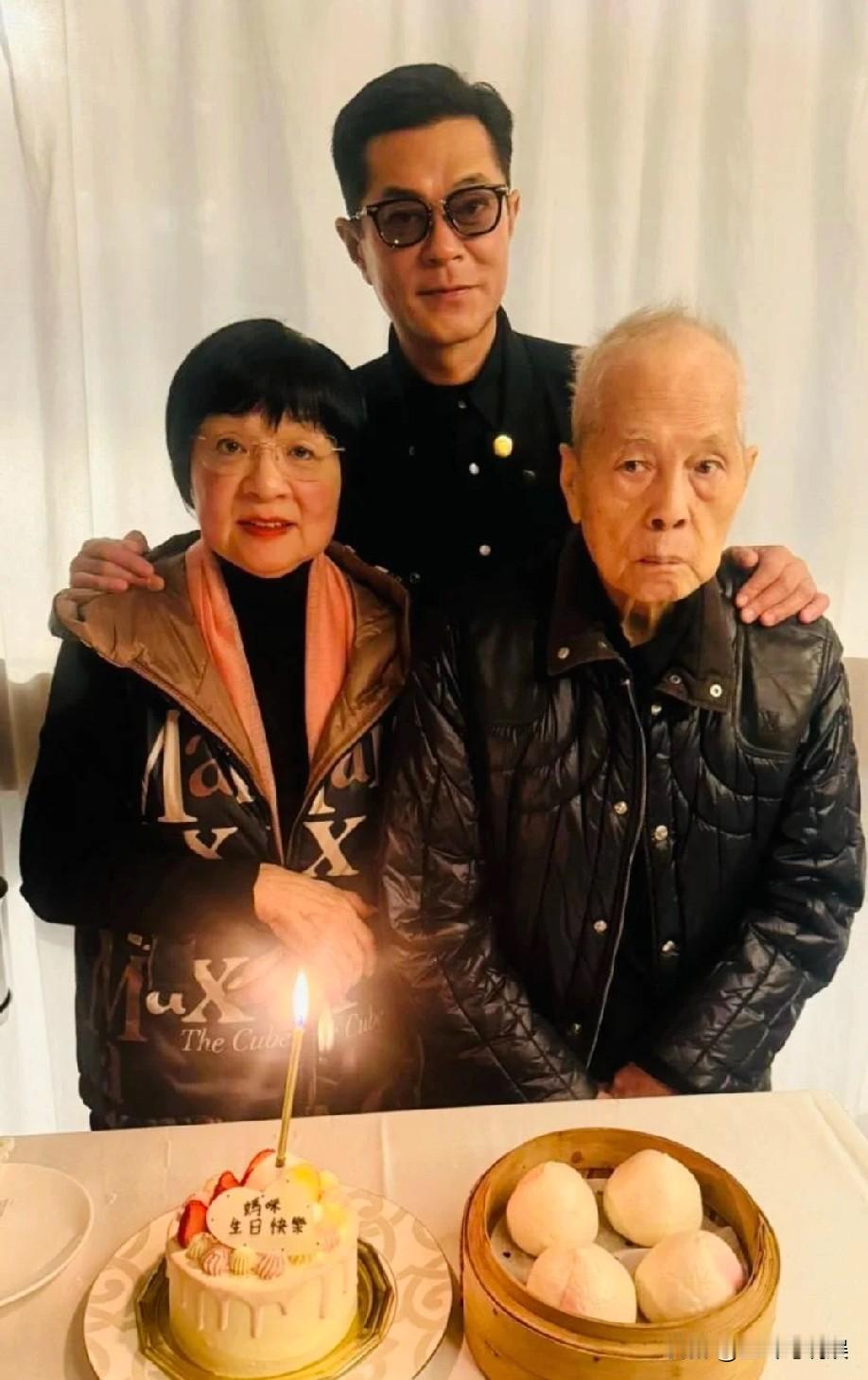 55岁古天乐晒全家福为妈妈庆生，他为妈妈准备了蛋糕和寿桃，古天乐两只手分别搭在父