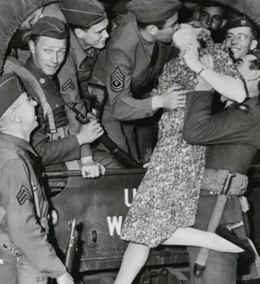 1940年，一名列兵将一位面容精致的女人高高举起，将她送给卡车上的大兵，大兵一把
