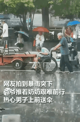 下雨了，大爷推着老伴在大雨中踯躅前行，一个热心的男子看到大爷大妈身上都淋湿了，马