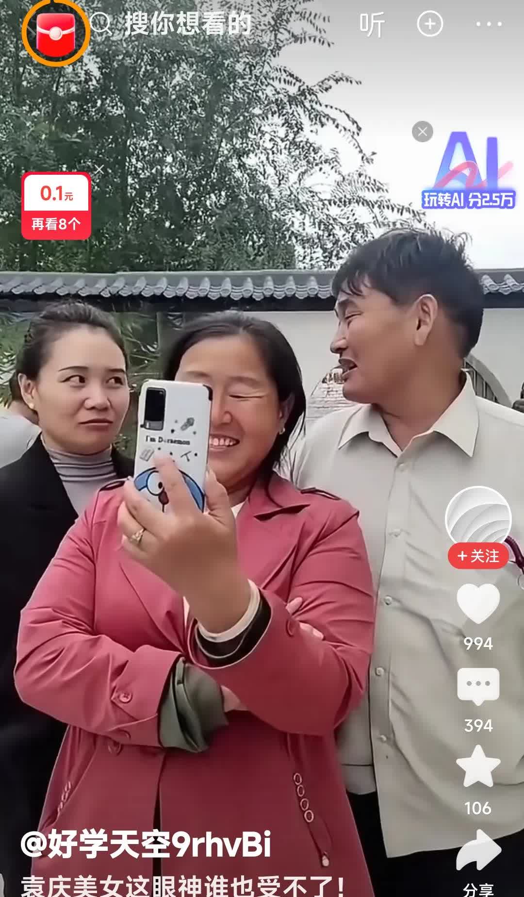 大衣嫂傻笑着在看着手机。袁庆和大衣哥在大衣嫂身后边儿，也在看大衣嫂的手机
