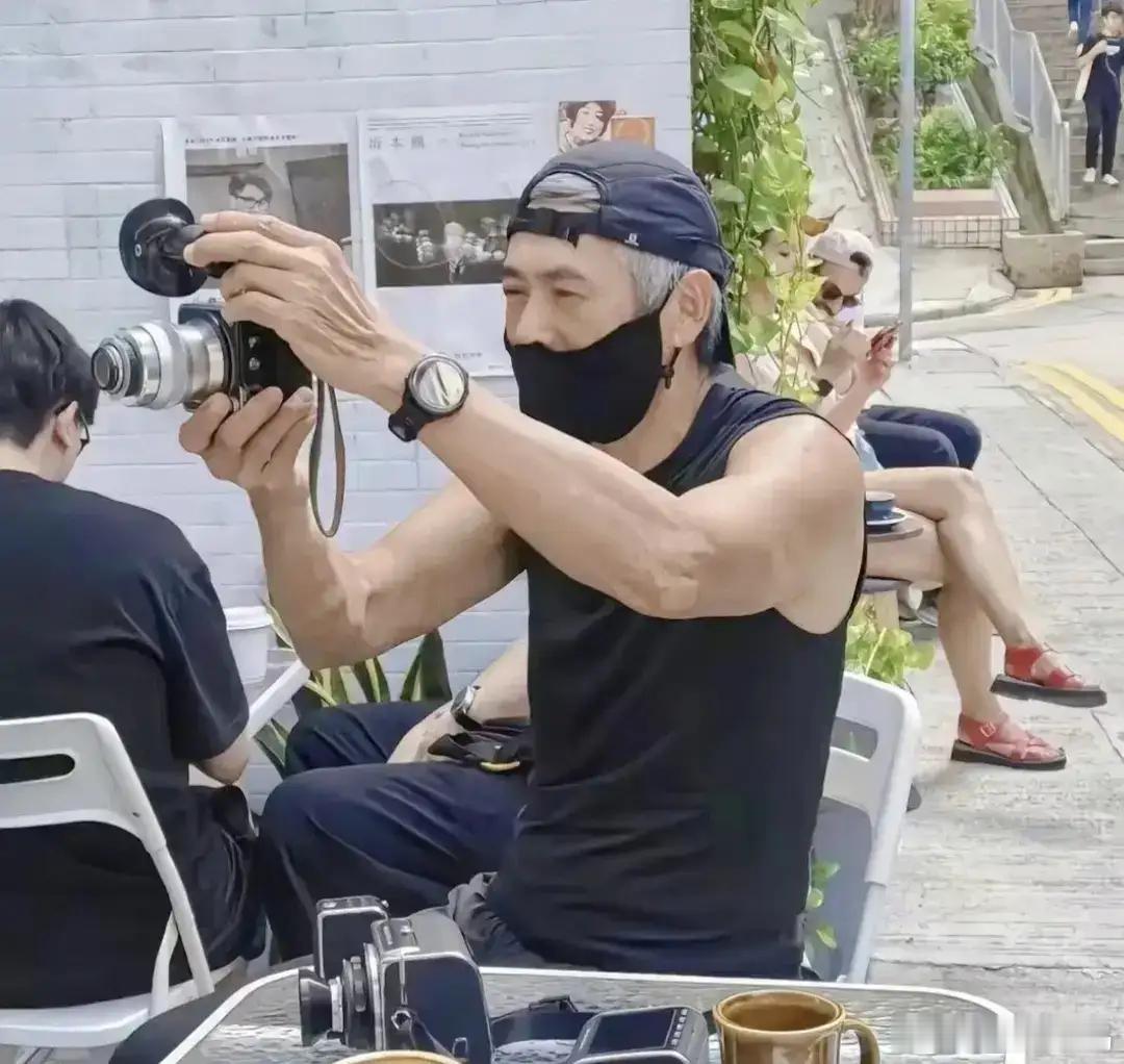 70岁的周润发在香港街头被偶遇，满头白发的他手持相机拍照，神情愉悦，状态轻松自在