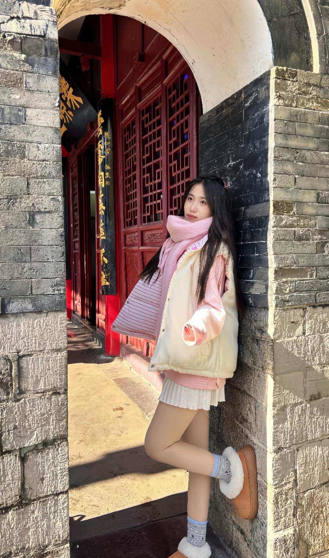 冬日暖阳下，少女倚靠红墙，粉白相间，甜美如画。