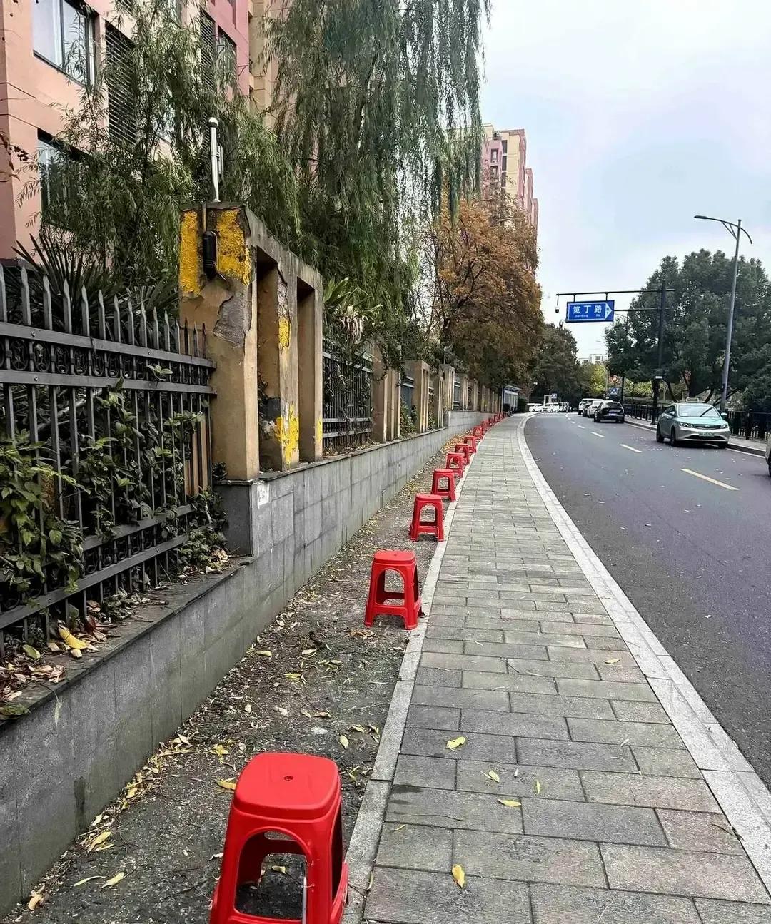杭州某小区人行道老被车堵，物业干脆搬来一排红色塑料凳，晚上横在路口，白天收起来，