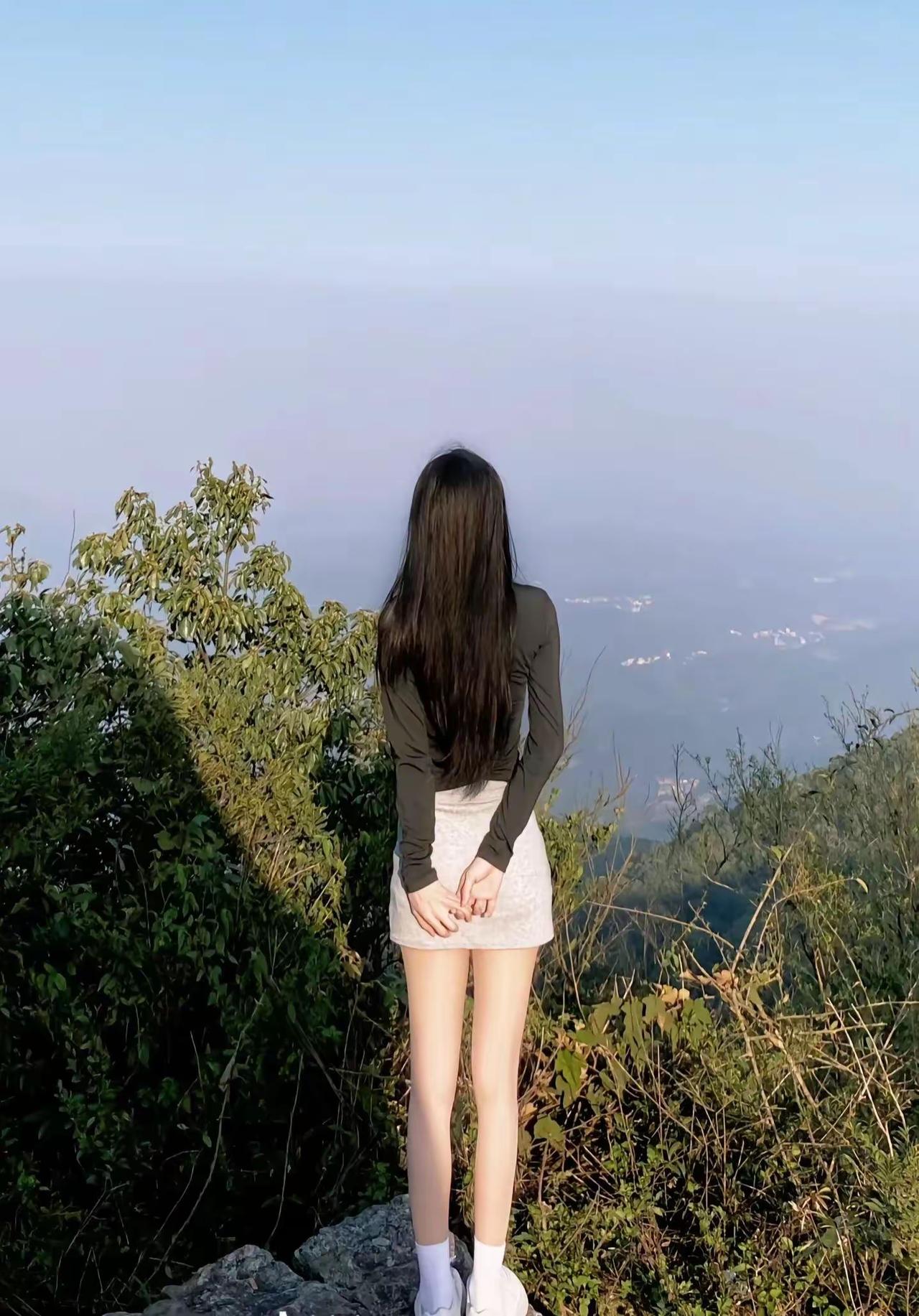长发女孩站在山顶眺望远方的风景。