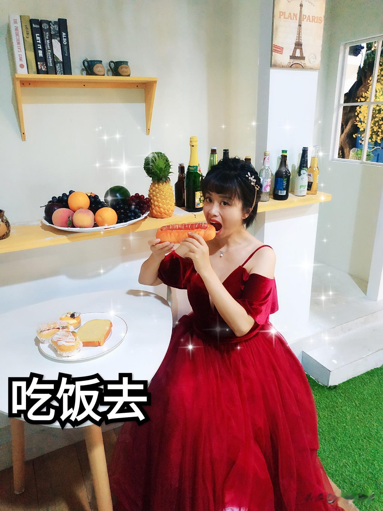一身华丽的酒红色露肩蓬纱礼服，优雅又隆重，和搞怪的动作形成有趣反差。背景是充满氛