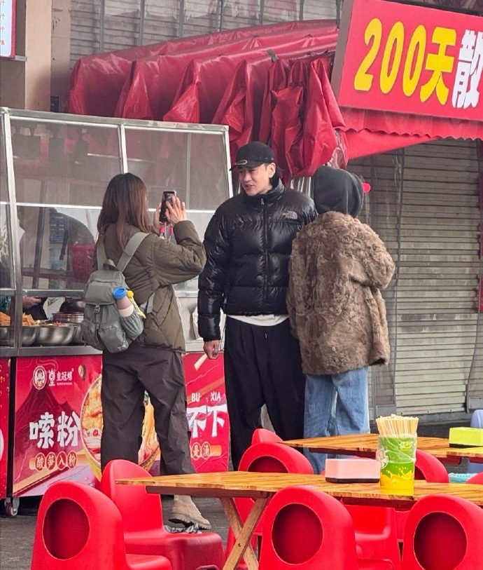 50岁何润东在柳州一家路边摊吃螺蛳粉，他穿着黑色羽绒服，身材高大健硕，看起来好年