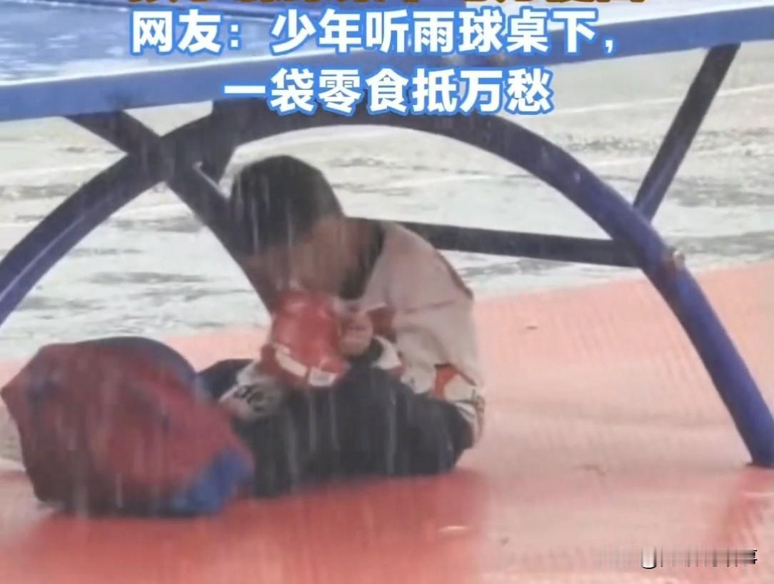 河南街头下起大雨，路人匆匆避雨，发现乒乓球桌下，一个孩子蜷在里面，一边躲雨一边啃