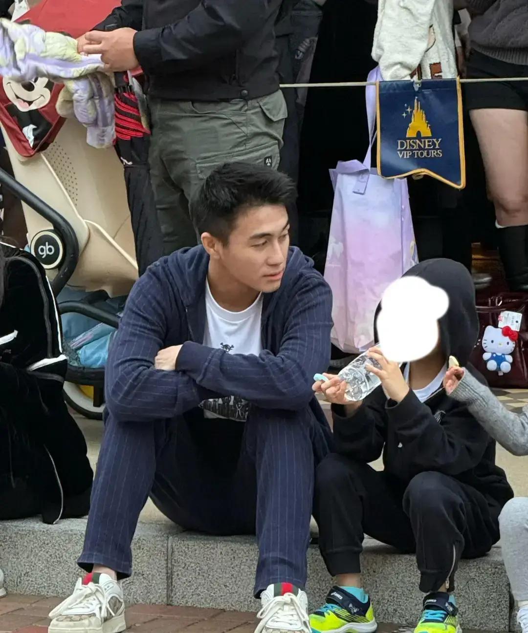 香港迪士尼门口，何猷君一家被拍到。儿子脚上是两百块的亚瑟士，他爸脚上却是四位数的