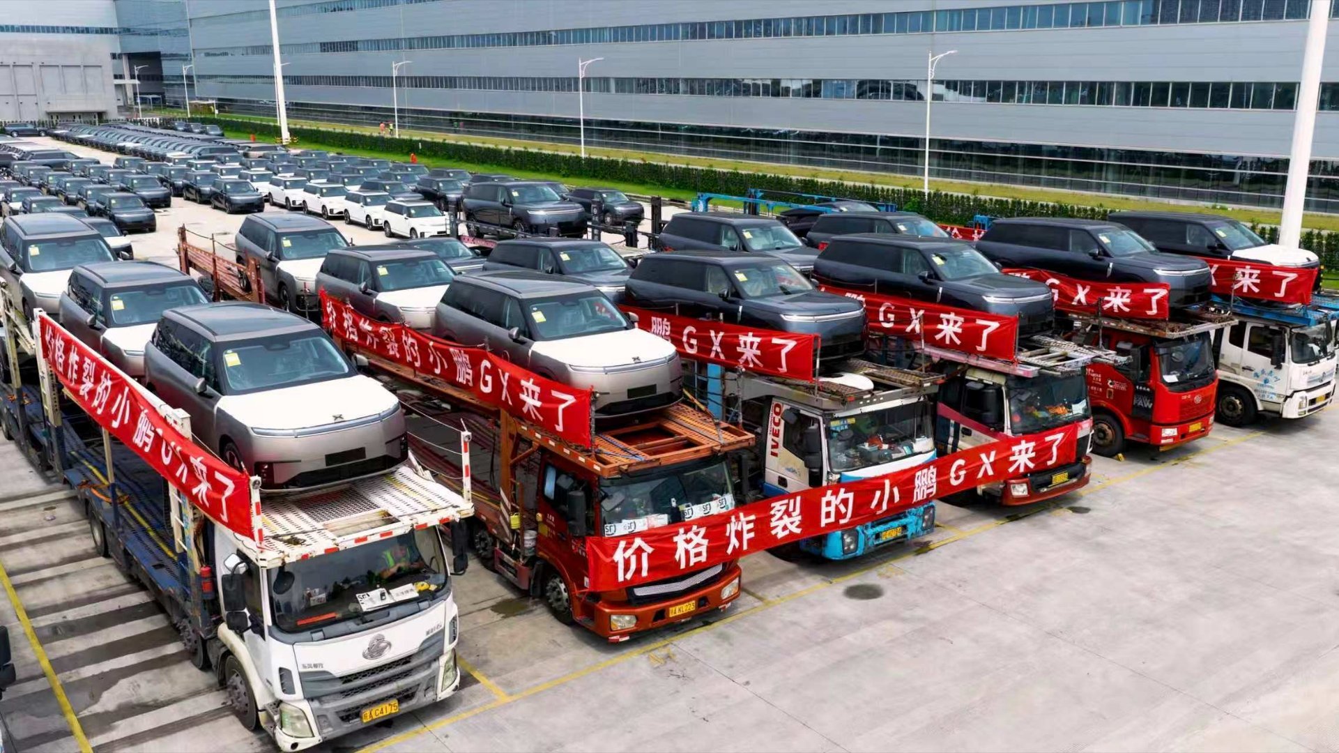停车场里全是整装待发的小鹏GX，板车上拉着“价格炸裂的小鹏GX来了”的...