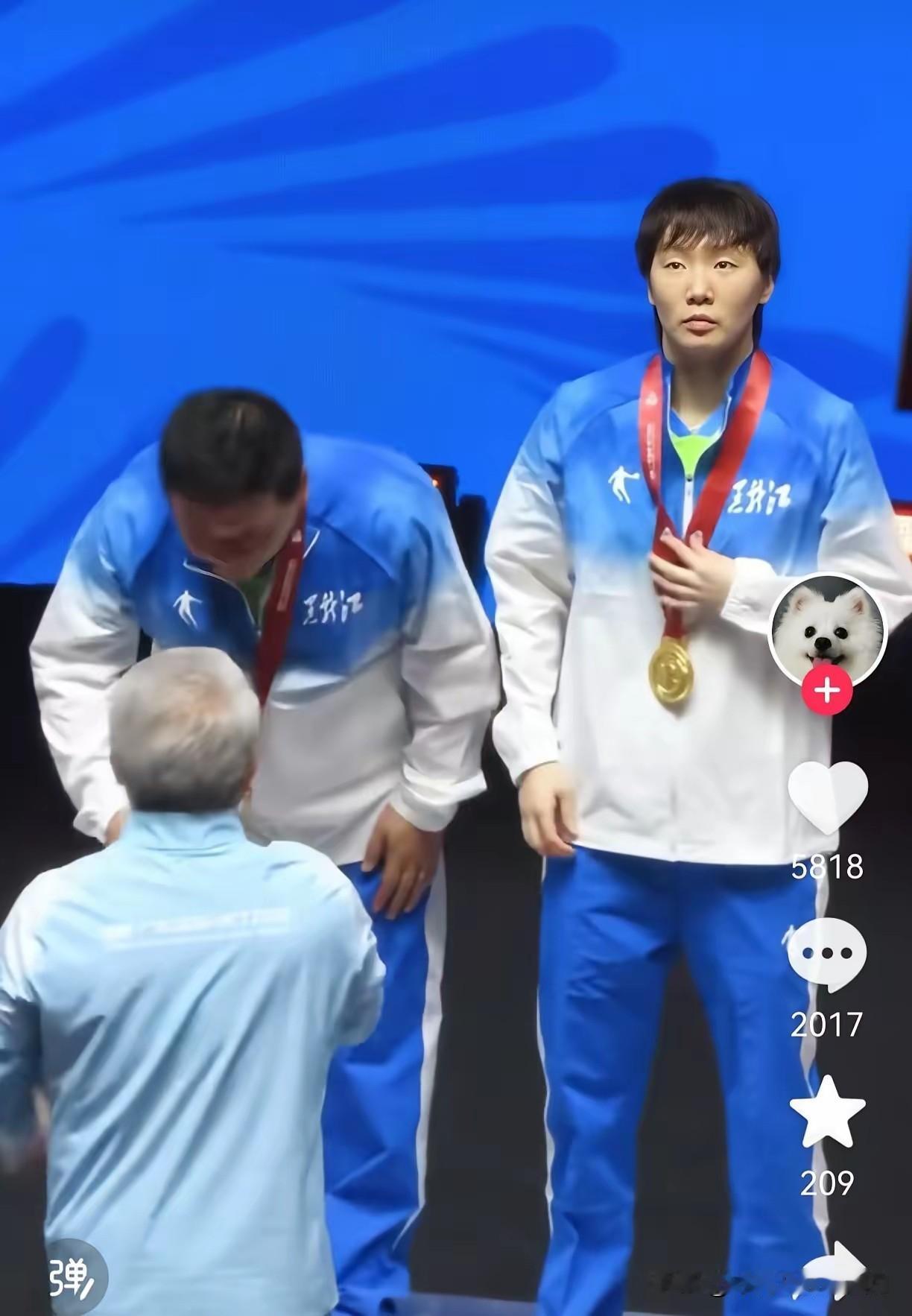 颁奖台是运动员享受荣誉的时刻。王曼昱刚打完一场激烈的比赛，拿到金牌。观众的喊声却