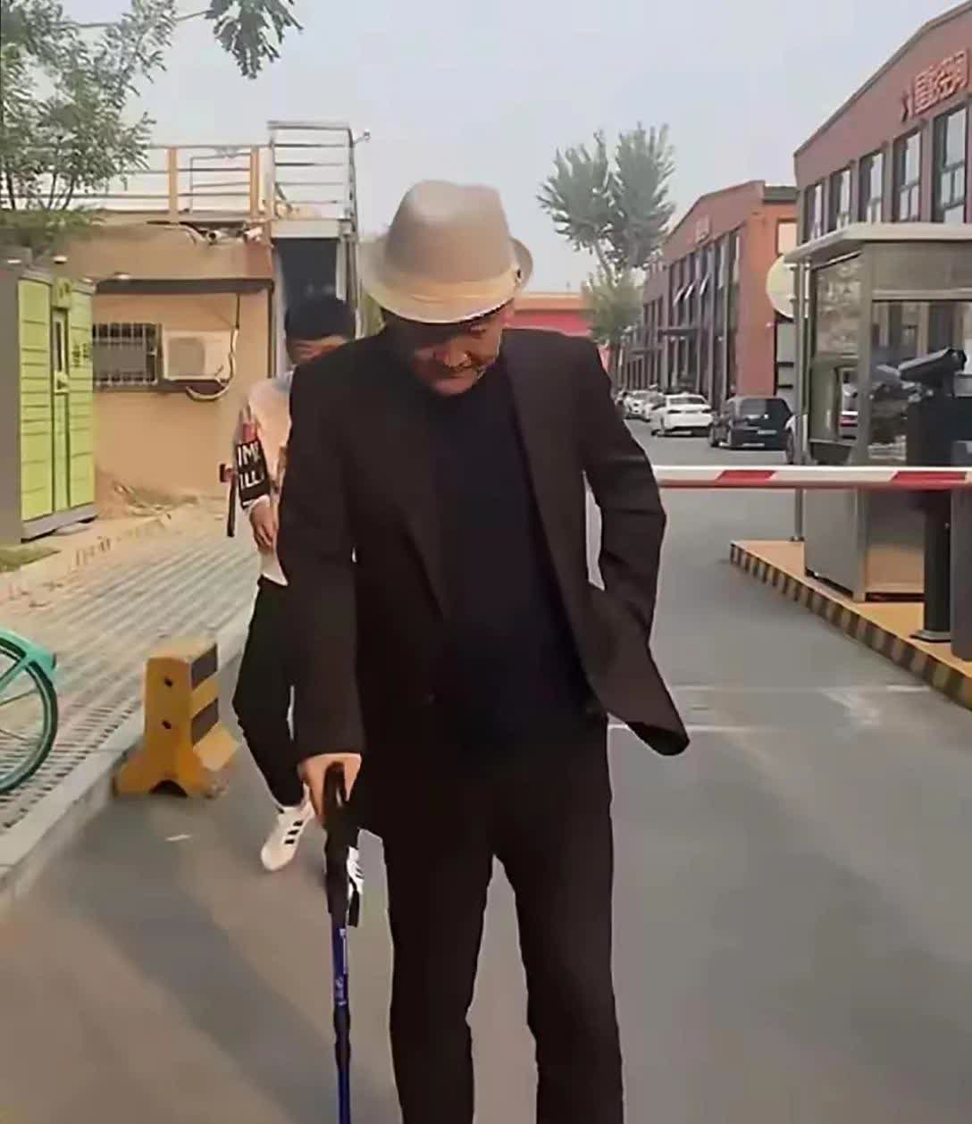 画面中的梁天体型偏瘦，穿搭讲究，气色红润，步履维艰，才66岁就拄拐杖了！！