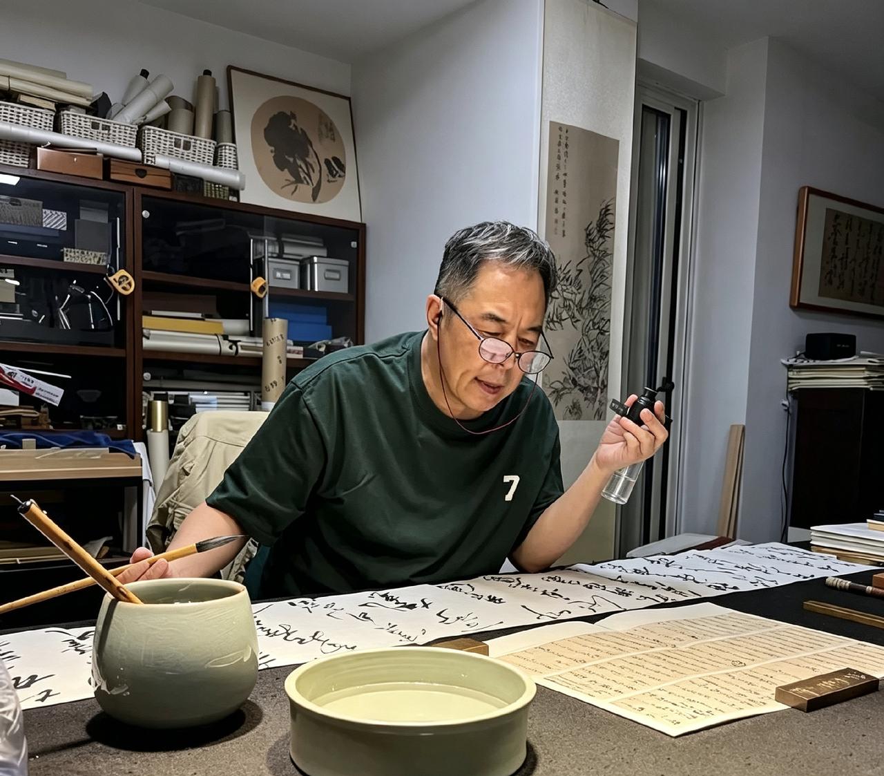 张铁林独坐书房练字，一手握烟斗，一手持毛笔，对照字帖凝神品读。满屋书法手稿，抛开