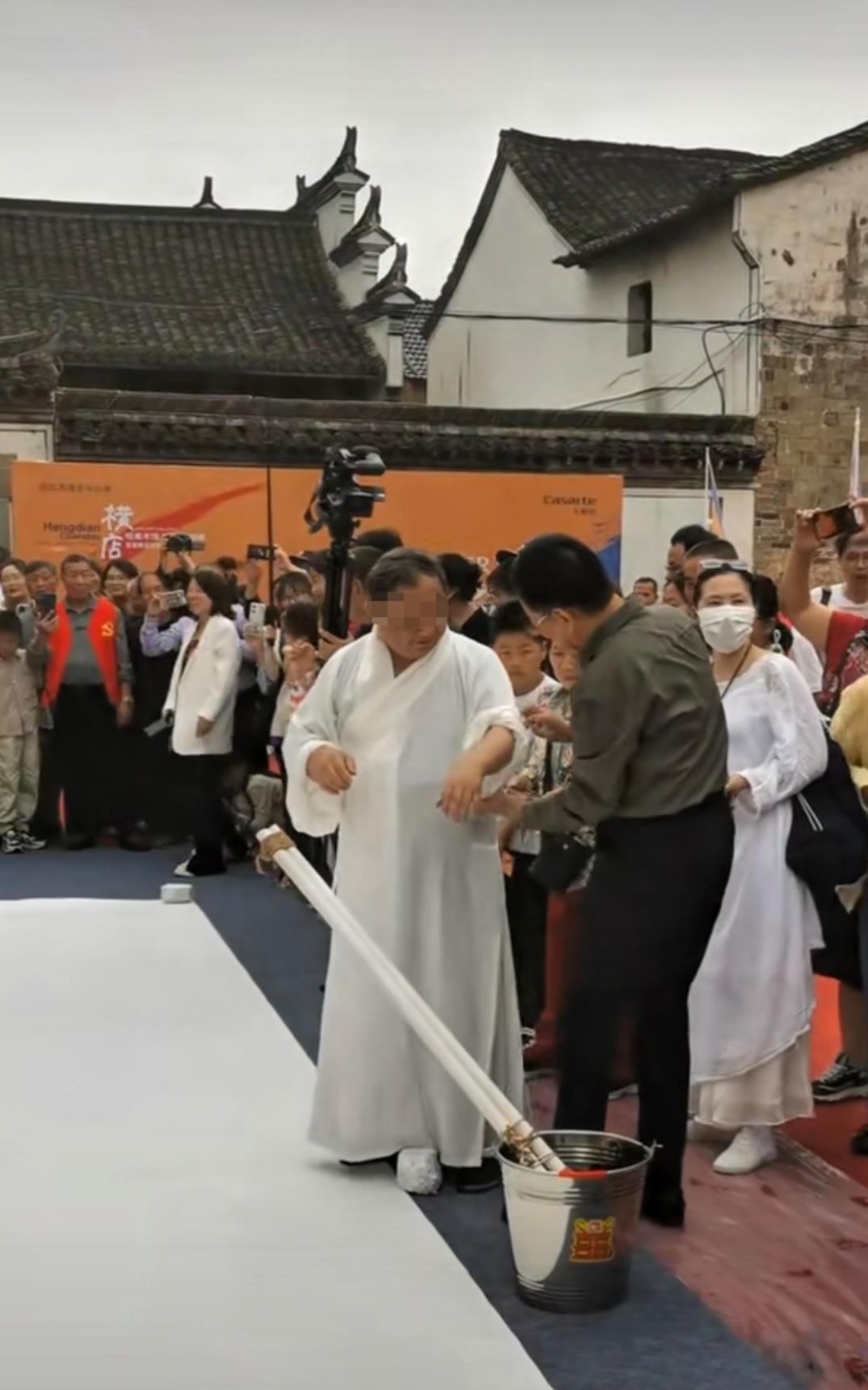 近日一位书画大师在景区表演书法，地上铺了一张巨型画布，周围围满了观看的游客，只见