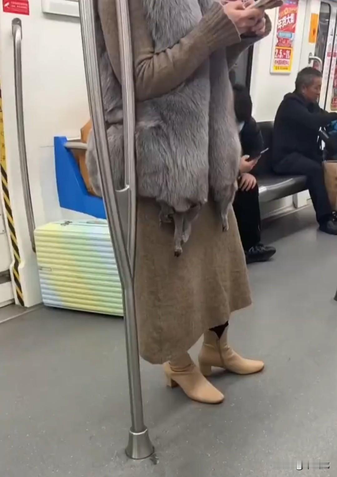 女子穿着皮草坐地铁，令人瞠目结舌的是，她这件灰色的皮草马甲，下摆竟然还垂着几条狐