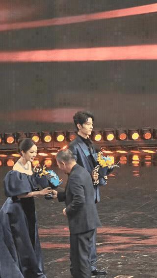 两个犟种在台上杠上了，一个直挺挺的一动不动，一个用脚一下一下踢着裙摆，一个非要站