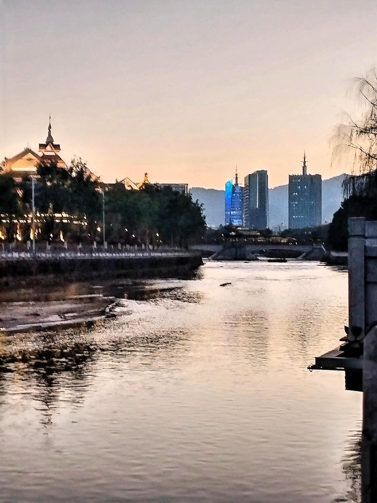 顺着湖畔小径前行，路边的花草在余晖与灯光的映照下，仿佛被赋予了独特的色彩。偶尔有