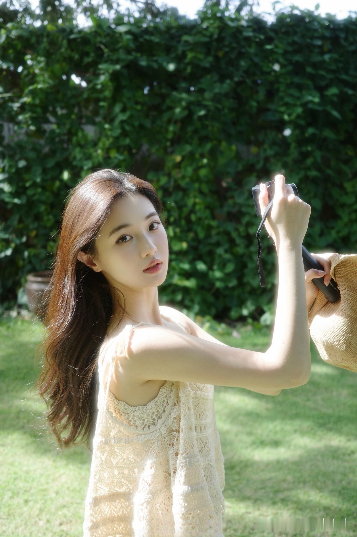 阳光洒落，少女在绿意盎然的庭院中，微笑着轻抚发丝，宛如一幅清新自然的夏日画卷。