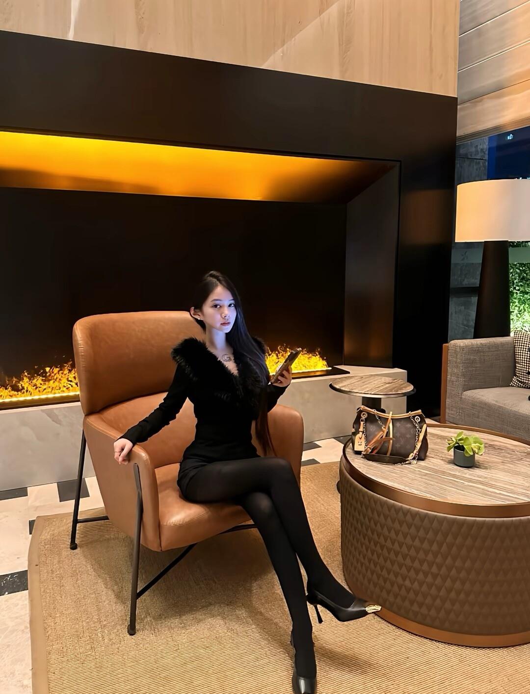 优雅黑衣女郎，手机轻抚，暖火映照，时尚气息扑面而来。