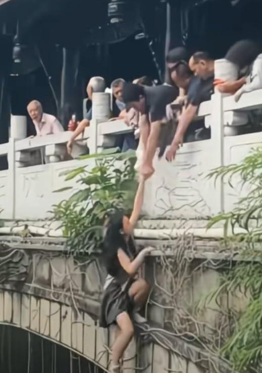 夏日景区一女子悬挂在桥梁外侧，游客上前搭救，最后还是落入水中，游客有的把绳子
