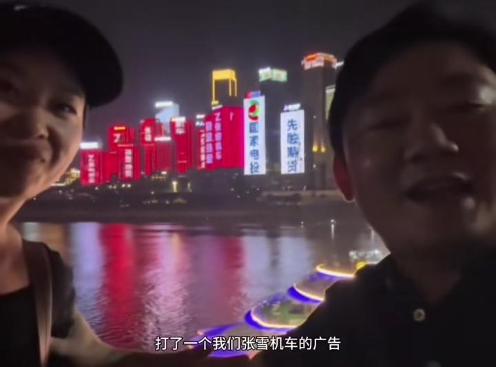 张雪带着老婆星姐来到重庆洪崖洞，满眼都是自家张雪机车的巨型广告牌，夫妻俩并肩看着