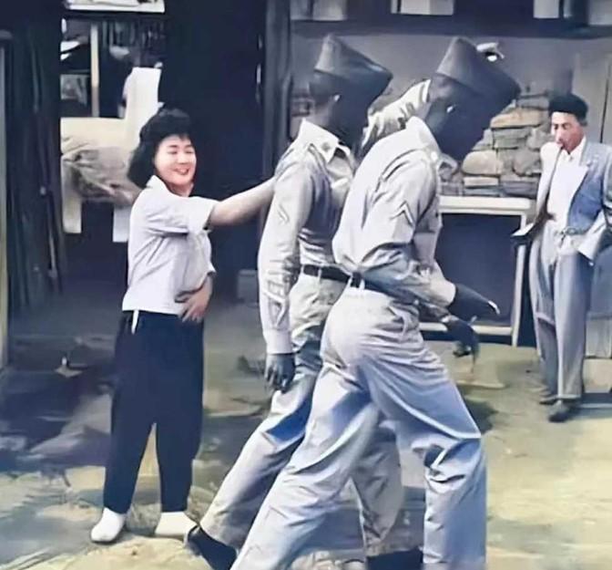 1952年，一名南朝鲜女子给两名美军做完服务后，当着老公的面热情地送大兵们离开。