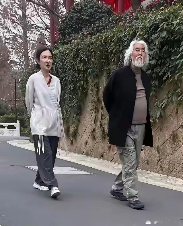 张纪中和夫人出门散步，两个人悠闲地走在路上。张纪中昂首挺胸走在前边，夫人跟