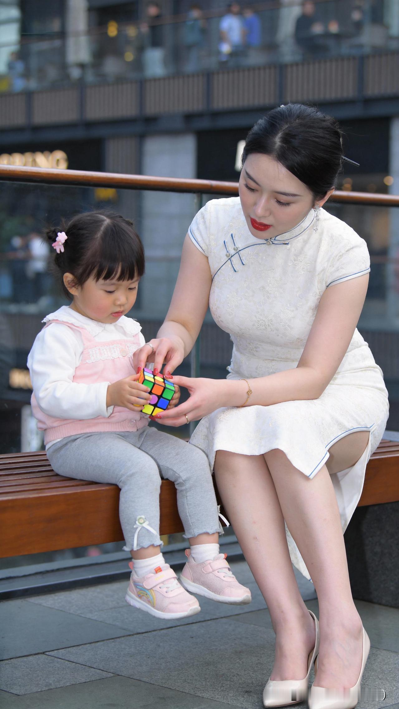 晚风轻软，小囡执魔方蹲于阶前钻研不休，暮色渐浓仍执着未竟，一旁母亲温柔守候，不催