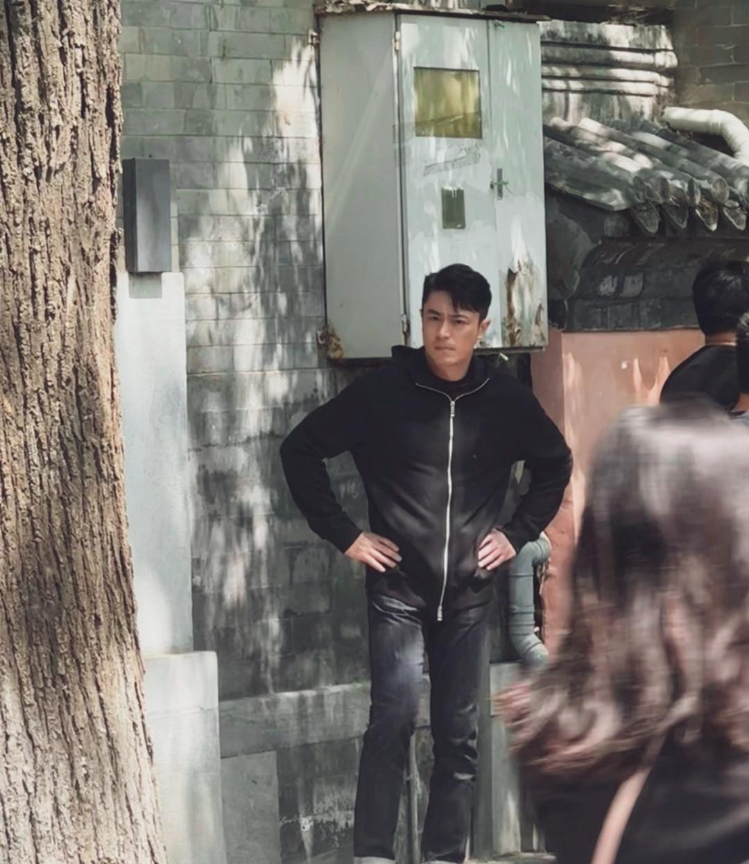 霍建华身穿黑色连帽卫衣，配黑牛仔裤，双手掐腰站在北京街头，五官立体硬朗，表情很凝