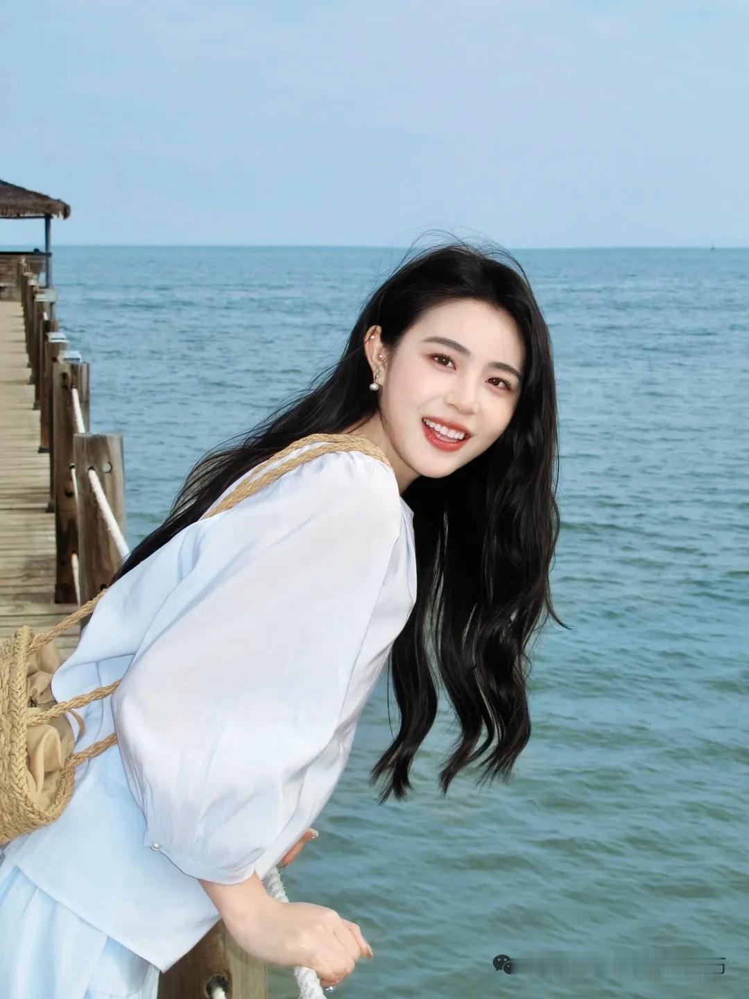 春日生活打卡季海边长发白衣少女倚立木桥，海风轻拂，观潮起潮落。