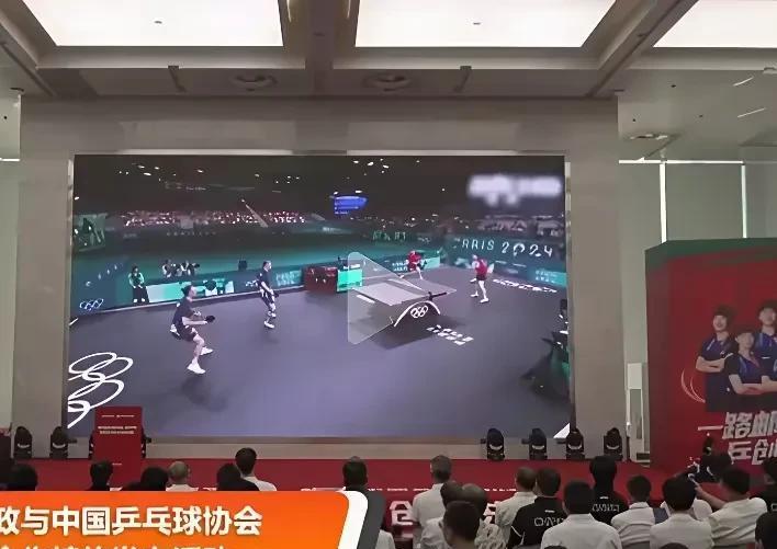 大屏上正在播放莎莎和王楚钦巴黎夺冠的画面，两个人都看的很认真，一脸严肃，可能秒回
