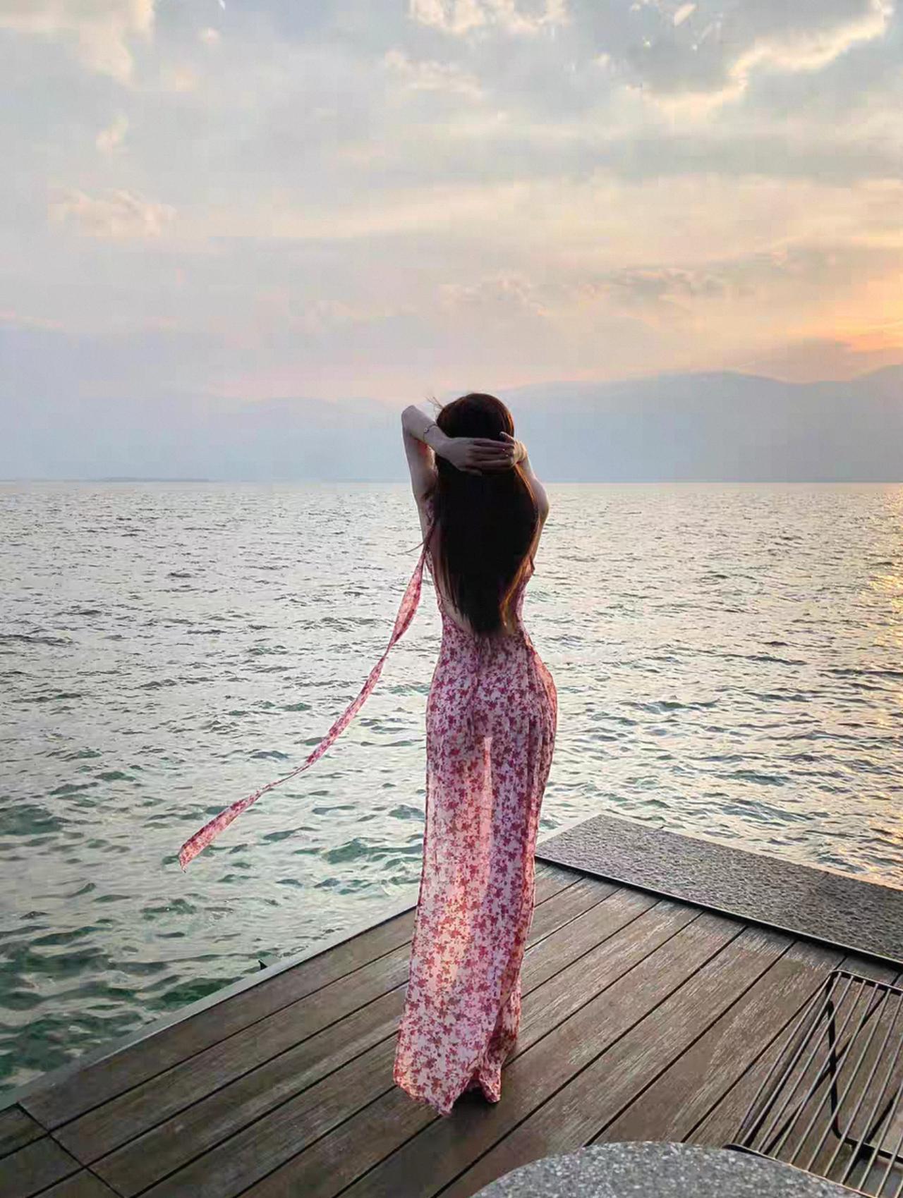 一袭透视长裙轻拂码头，裙摆摇曳间，曼妙身姿若隐若现，与海边余晖韵味相得益彰。