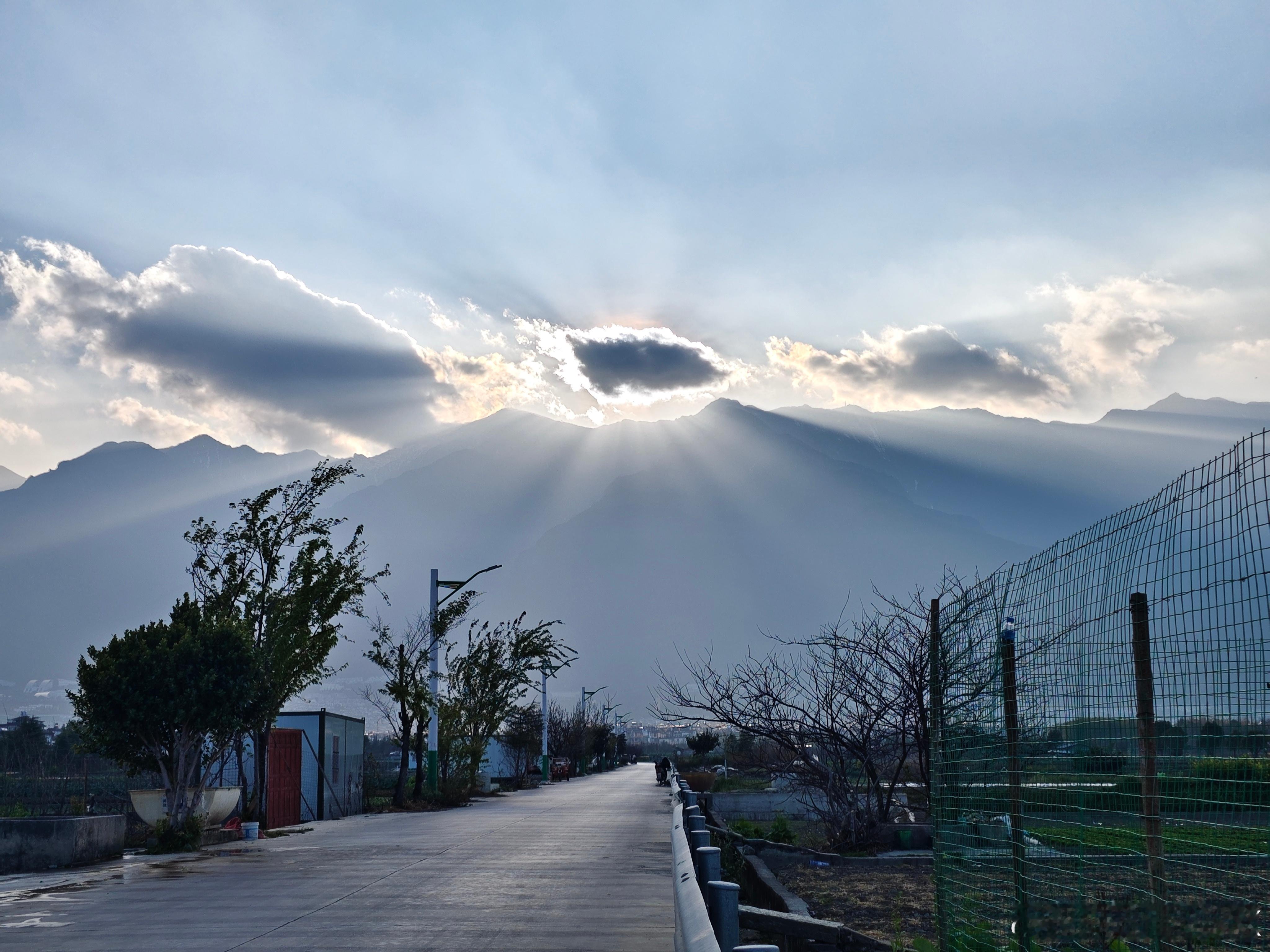 夕阳下的苍山，阳光穿透云层洒在大地上，马路，田地，耕种的人.....大理是国内最